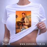 Футболка Іван Франко білого кольору, розкладена на поверхні. Принт зображає чоловіка в світлому костюмі, який читає книгу, на фоні оранжевого заходу сонця. На футболці видно етикетку з зеленим шнурком, що додає акценту. Фон нейтральний, світло-сірий.