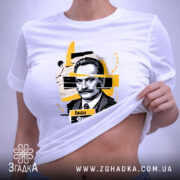 Футболка Іван Франко, біла, на столі, складена, з принтом портрета Івана Франка, фон світло-сірий, деталі принта в жовтих і чорних кольорах.