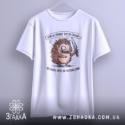 Футболка Їжак не ніжний, біла, зображена з легким нахилом, фон світло-сірий, принт з їжаком з ножем, текст зверху та знизу принта.