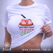 Футболка Їжте сало, біла, складена на поверхні, фон світлий, принт з милим шматком сала на дерев'яній дошці з ножем, текст під принтом яскравий і веселий.