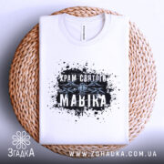 Футболка Храм святого Мавіка, біла, складена на плетеній основі, фон світло-сірий, принт з чорними плямами та написом 'Храм святого Мавіка'.