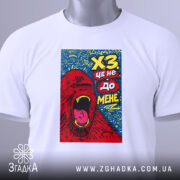 Футболка ХЗ білого кольору, зображена зверху, фон світлий, принт з червоним ведмедем, що кричить, на синьому фоні, з зеленим ярликом.