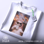 Футболка кіт спокій, біла футболка на столі, з принтом кота в окулярах, що тримає чашку, на фоні з вогнем і вибухами, ракурс зверху, з етикеткою на шнурку.