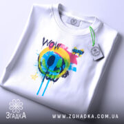 Футболка Кольоровий поп арт, біла, на столі, ракурс зверху, фон світлий, принт з кольоровим смайлом та написом 'WOW', яскраві кольори: жовтий, зелений, блакитний, рожевий, чорний, етикетка з зеленим шнурком.