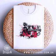 Футболка Королева випускного білого кольору, складена на плетеній кошику, фон світлий, принт з чорними та червоними елементами, що зображає силует дівчини в короні.