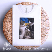 Футболка котяча банда, біла, з верхнього ракурсу, на плетеній кошику, фон світло-сірий, принт з двома котами, один з яких тримає татуювальну машинку, на фоні жовто-блакитний прапор.