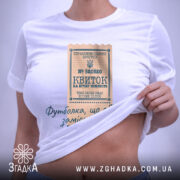 Футболка квиток, біла, на плоскій поверхні, фон світлий, принт у вигляді квитка з текстом, прикріплена етикетка з зеленим шнурком.