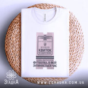 Футболка квиток на відпочинок, біла, складена на плетеній кошику, фон натуральний, принт у вигляді квитка з текстом 'Квиток на відпочинок', видно етикетку на комірці.