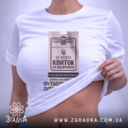 Футболка квиток на відпочинок, біла, знята зверху, фон світло-фіолетовий, принт у вигляді квитка з текстом 'Квиток на відпочинок', на комірці є етикетка.