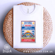 Футболка квиток у найкраще життя. Біла футболка, складена на плетеній кошику, з принтом у вигляді квитка, що містить кольорові деталі. Фон світлий, з м'яким освітленням.