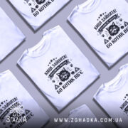 Футболка киця зайнята, біла, на моделі, з легким ракурсом спереду, фон світло-фіолетовий, принт чорного кольору з зображенням кота та текстом.