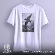 Футболка ластівка над Києвом арт принт, біла футболка підвішена на вішалці, ракурс спереду, фон світло-сірий, принт зображує ластівку на фоні Київських будівель у чорно-білому стилі.