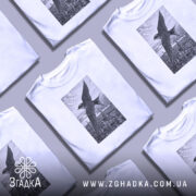 Футболка ластівка над Києвом арт принт, біла футболка на чоловікові, ракурс з близької відстані, фон світло-фіолетовий, принт зображує ластівку на фоні Київських будівель у чорно-білому стилі.