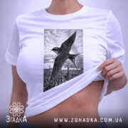Футболка ластівка над Києвом арт принт, біла футболка складена на поверхні, ракурс зверху, фон світло-сірий, принт зображує ластівку на фоні Київських будівель у чорно-білому стилі, з етикеткою зеленого кольору.