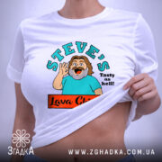 Футболка Лава Чікен, біла, на плоскій поверхні, з близьким ракурсом, фон світло-сірий, принт з персонажем, що махає рукою, текстом 'STEVE'S Tasty as hell!' та логотипом 'Lava Chicken', з етикеткою на комірці.