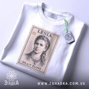 Футболка Леся Українка, біла, зображена зверху на плоскій поверхні, фон світло-сірий, принт у вигляді поштової марки з портретом Лесі Українки, текст 'SILA V SLOVI' під зображенням, на футболці прикріплена етикетка з зеленим шнурком.