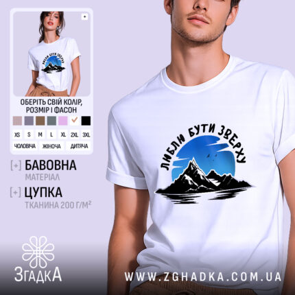 Футболка люблю бути зверху, біла, на моделі, фон світло-фіолетовий, принт з горами та небом, текст чорного кольору.