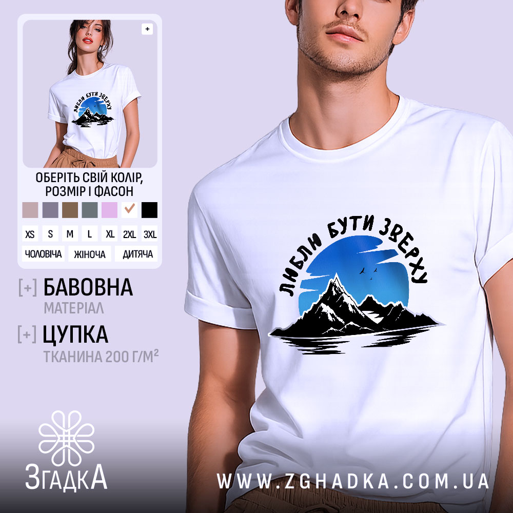 Futbolka Liubliu Buty Zverkhu Stylnyi Vybir Dlia Kozhnoho 1 Футболка люблю бути зверху, біла, на моделі, фон світло-фіолетовий, принт з горами та небом, текст чорного кольору.