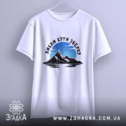 Футболка люблю бути зверху, біла, на вішалці, фон світло-сірий, принт з горами та небом, текст чорного кольору.