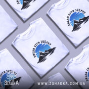 Футболка люблю бути зверху, біла, на моделі, фон світло-фіолетовий, принт з горами та небом, текст чорного кольору.