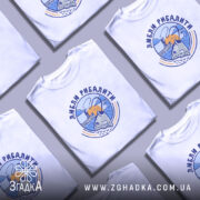 Футболка люблю рибалити, біла, зображена на молодому чоловікові, фон світло-фіолетовий, принт з рибою та рибалкою на фоні заходу сонця.