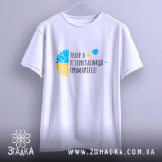 Футболка майбутньої пʼятикласниці білого кольору, підвішена на вішалці. Принт з жовто-блакитним соняшником та текстом "Тепер я п'ятікласниця – тримайтеся!" чітко видимий. Фон ніжно-фіолетовий, що створює м'яку атмосферу.