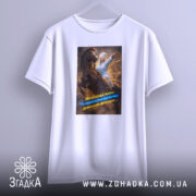 Футболка мама головнокомандувачка, білого кольору, підвішена на вішалці, принт з жінкою в халаті на коні, що вказує вперед, з яскравими кольорами та текстом, фон світлий.