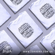 Футболка мені завжди є що додати. Біла футболка на моделі, з коротким рукавом, з чорним принтом на грудях, що містить текст. Модель позує на світло-сірому фоні, з легким макіяжем і розпущеним волоссям.