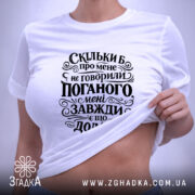 Футболка мені завжди є що додати. Біла футболка, складена на столі, з чорним принтом, що містить текст. На футболці видно етикетку, а фон світло-сірий, що підкреслює чистоту дизайну.