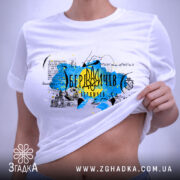 Футболка Мій Бердичів, біла, на плоскій поверхні, з видимим принтом, фон світло-сірий, принт з жовтими та блакитними кольорами, з написом 'Бердичів' та архітектурними елементами.