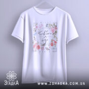 Футболка Мода це життя, біла футболка, підвішена на вішалці, фон світло-сірий, принт з квітами та написом 'Fashion is Life' розташований у центрі.