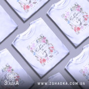 Футболка Мода це життя, біла футболка з коротким рукавом, зображена на моделі з легким макіяжем, фон пастельного кольору, принт з квітами та написом 'Fashion is Life' у центрі.