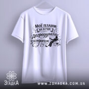 Футболка мої плани на вечір. Біла футболка, підвішена на вішалці, зображена спереду. На фоні світлий однотонний колір. Принт чорного кольору з написом "Мої плани на вечір: деградувати з комфортом" та ілюстрацією сидячої фігури з попкорном.