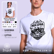 Футболка моя душа гори. Біла футболка з коротким рукавом, зображена на молодій людині, що позує з легким усмішкою. Принт на футболці чорного кольору, з елементами гір, сонця, лісу та рюкзака, що створює атмосферу пригод. Фон ніжно-фіолетовий, що підкреслює яскравість дизайну.