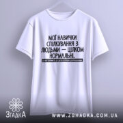 Футболка Моя терпимість, біла, підвішена на вішалці, фон світло-сірий, принт чорного кольору з текстом на українській мові, розташований по центру.