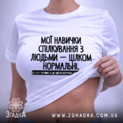 Футболка Моя терпимість, біла, лежить на плоскій поверхні, фон світло-сірий, принт чорного кольору з текстом на українській мові, етикетка з зеленим шнурком.