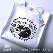 Футболка Моя тиша, біла, на плоскій поверхні, з етикеткою, фон світло-сірий, принт з зображенням сплячого лиса в обрамленні рослинних мотивів і сердець.