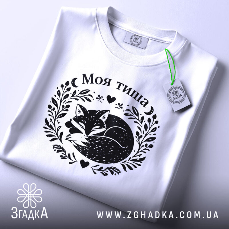 Футболка Моя тиша, біла, на плоскій поверхні, з етикеткою, фон світло-сірий, принт з зображенням сплячого лиса в обрамленні рослинних мотивів і сердець.