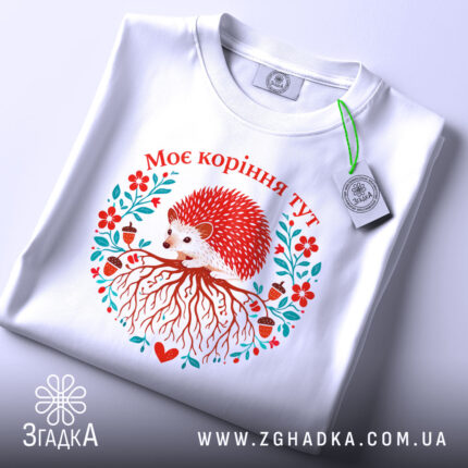 Футболка моє коріння тут, біла, зображена на плоскій поверхні, фон світло-сірий, принт з їжаком, червоними квітами та корінням, текст "Моє коріння тут" над принтом, з етикеткою.