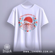 Футболка моє коріння тут, біла, підвішена на вішалці, фон світло-сірий, принт з їжаком, червоними квітами та корінням, текст "Моє коріння тут" над принтом.