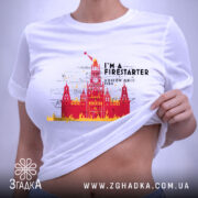 Футболка москва у вогні, складена футболка на білому фоні, ракурс зверху, принт з червоним і жовтим зображенням Кремля з написом 'I'M A FIRESTARTER' та 'MOSCOW ON FIRE', етикетка на футболці.