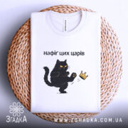 Футболка нафіґ цих царів, біла, складена на кошику, з принтом чорного кота, який піднімає лапу до корони, фон світло-фіолетовий, деталі принта чіткі, текст чорний.