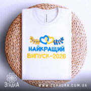 Футболка найкращий випускний 2026, біла, складена на плетеній основі, фон світло-блакитний, принт яскравий, з сердечками та листям, напис великими літерами.