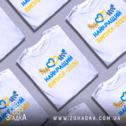 Футболка найкращий випускний 2026, біла, на моделі, з легким усмішкою, фон світло-фіолетовий, принт з жовтими та синіми елементами, напис великими літерами, з сердечками та листям.