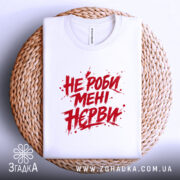 Футболка не роби мені нєрви, біла, складена на плетеній кошику, фон світло-сірий, принт червоний з агресивним шрифтом, текст займає центральну частину, видно комірець.