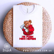 Футболка не роби мені нєрви. Біла футболка, складена на плетеній основі, ведмідь в червоному капюшоні з сокирою, текст "НЕ РОБИ МЕНІ НЕРВИ!" під малюнком, на фоні світлого кольору.