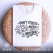 Футболка Не стресуй мені мозок. Біла футболка, складена на плетеній кошику, з видимим принтом чорного кольору. Текст 'DON'T STRESS мені мозок' та малюнок мозку. Фон світло-сірий.