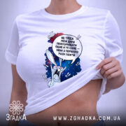 Футболка Не треба повторювати. Біла футболка, складена на столі, з принтом кролика на космічному фоні, текстом зверху. На футболці є етикетка з зеленим шнурком, фон світлий.