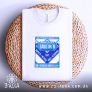 Футболка нічого не злипнеться, біла, зображена зверху, на плоскій поверхні з плетеним елементом, фон світлий, принт у синіх відтінках з текстом і графічними елементами.