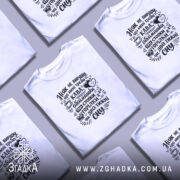 Футболка ніяк не вирішу що треба, біла, на моделі, фон світло-фіолетовий, принт чорний з текстом про каву та обіймашки.